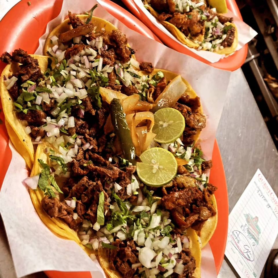 Two red plates filled with Tacos Acambaro's Mexican tacos, topped with meat, onions, cilantro, and lime.