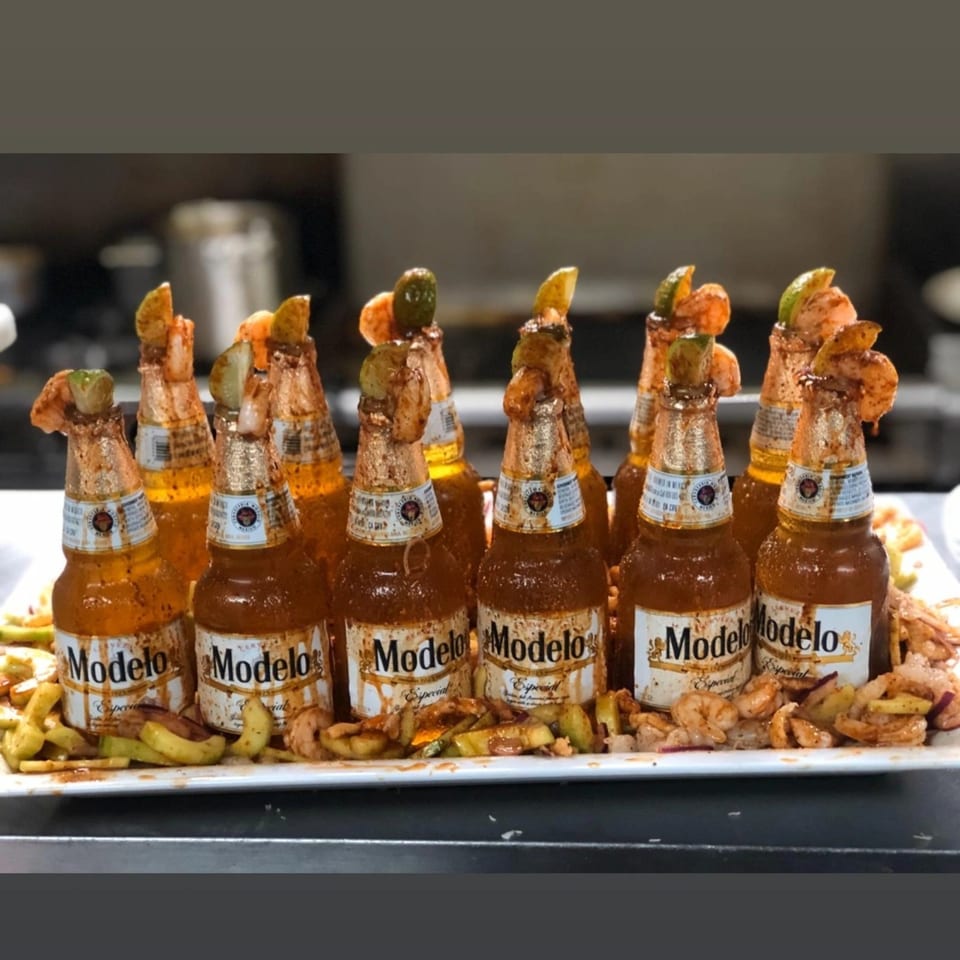 A platter of Modelo beer bottles, each garnished with shrimp, lime, and spices.