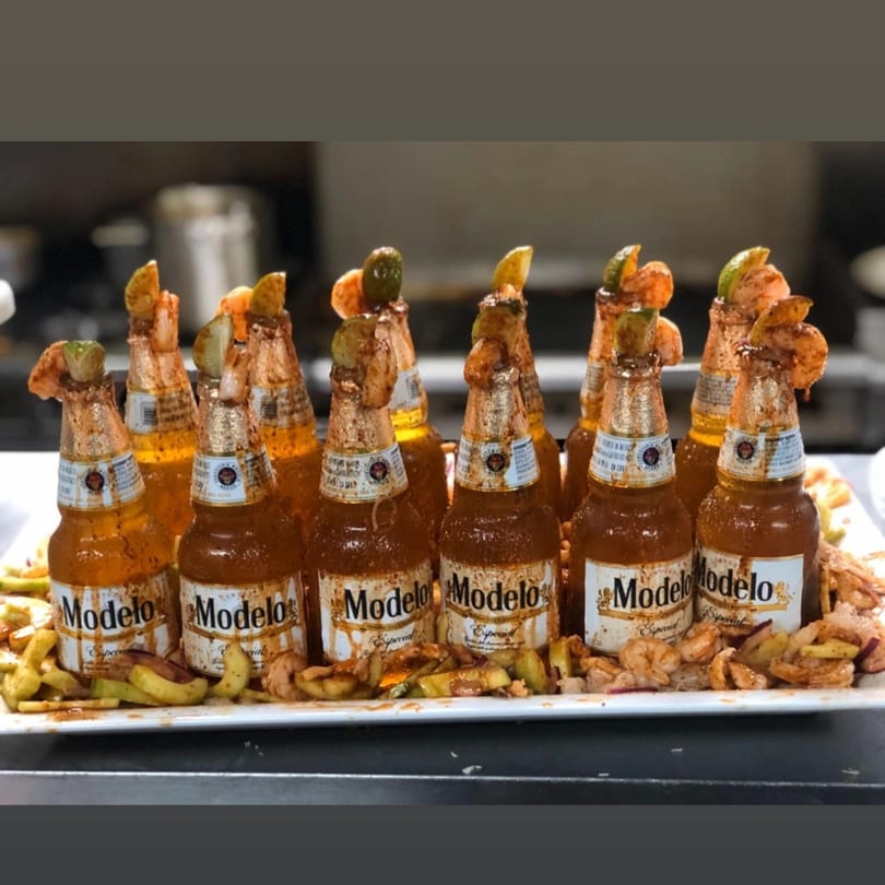 A platter of Modelo beer bottles, each garnished with shrimp, lime, and spices.