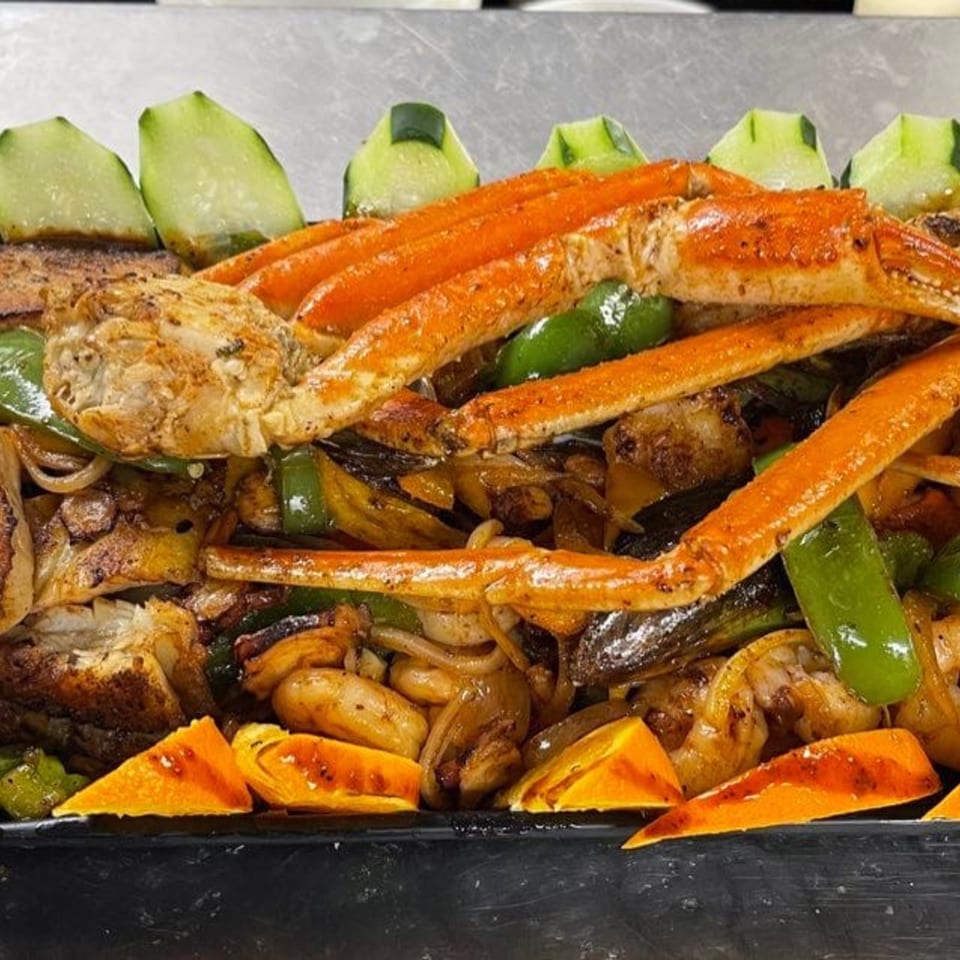 A close-up of a seafood dish with crab legs, shrimp, vegetables, and cucumber slices.