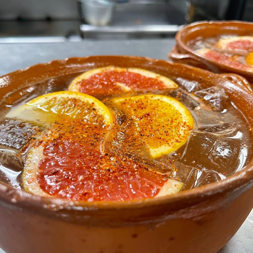 Mexican drink in a clay pot with grapefruit, orange slices, and chili powder.
