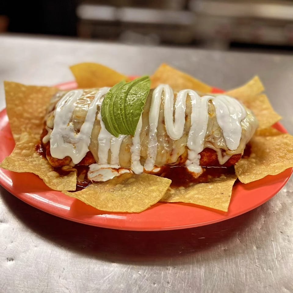 A Tacos Acambaro burrito covered in white sauce and avocado slices, surrounded by tortilla chips.